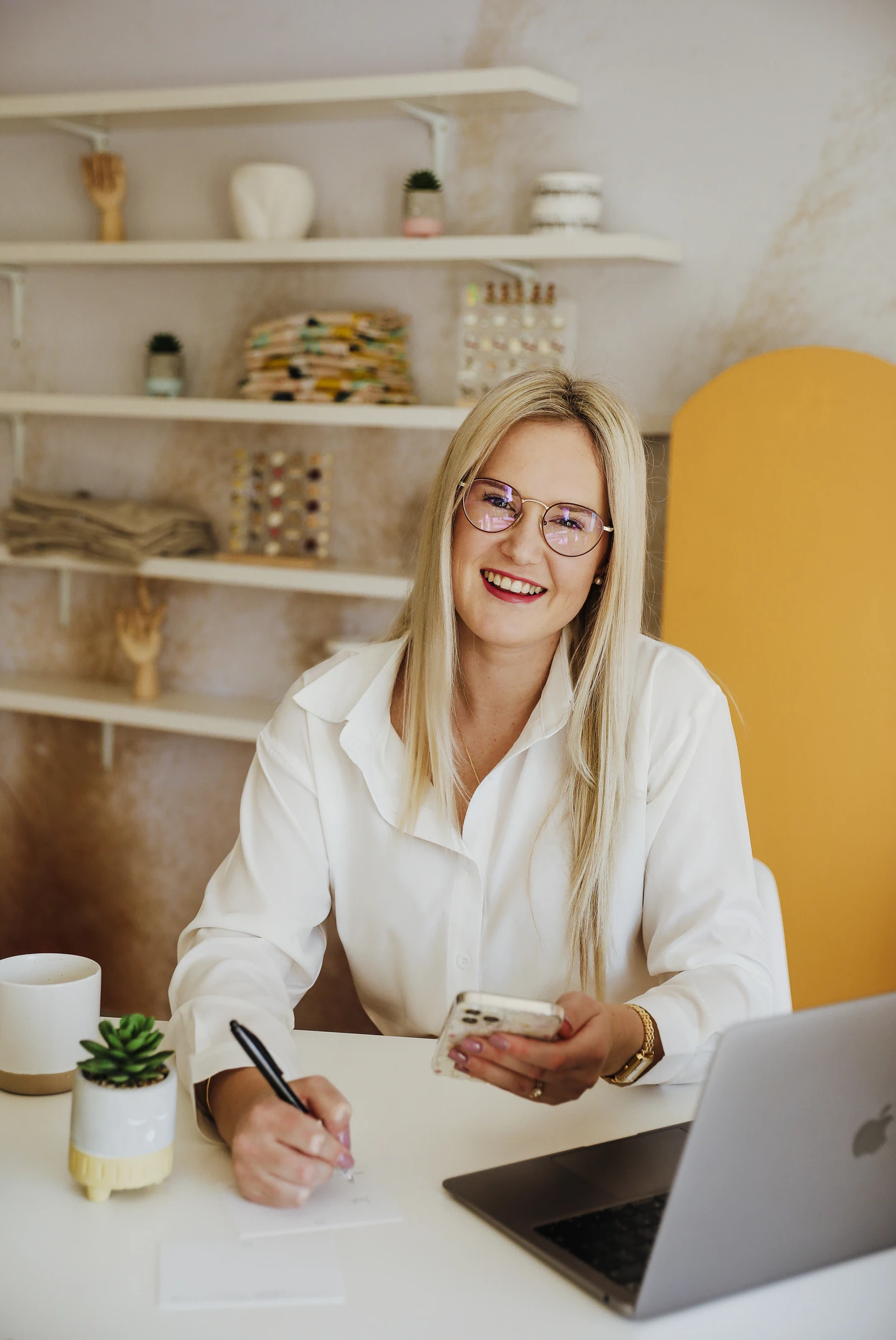 Smiling blonde woman working at modern desk with laptop and phone.